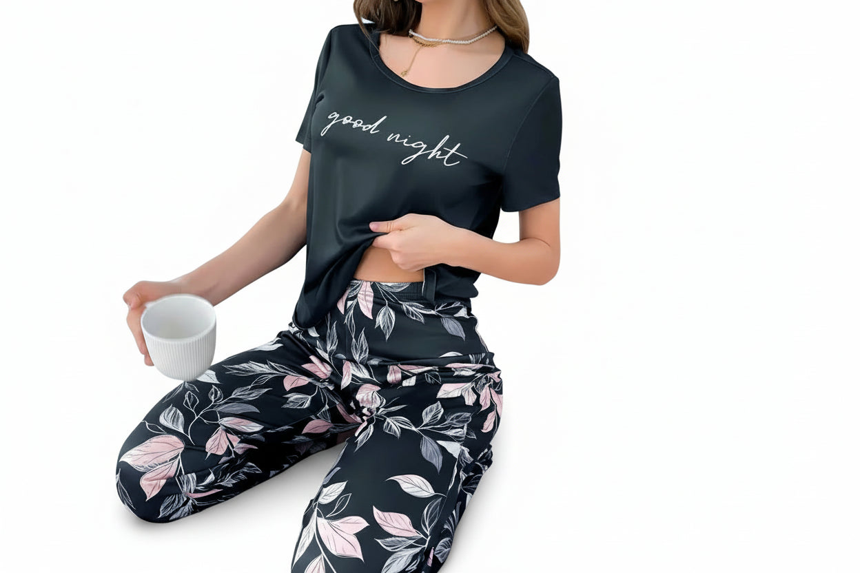 Person wearing a black 'good night' t-shirt and leaf-patterned pants, sitting on a bed.