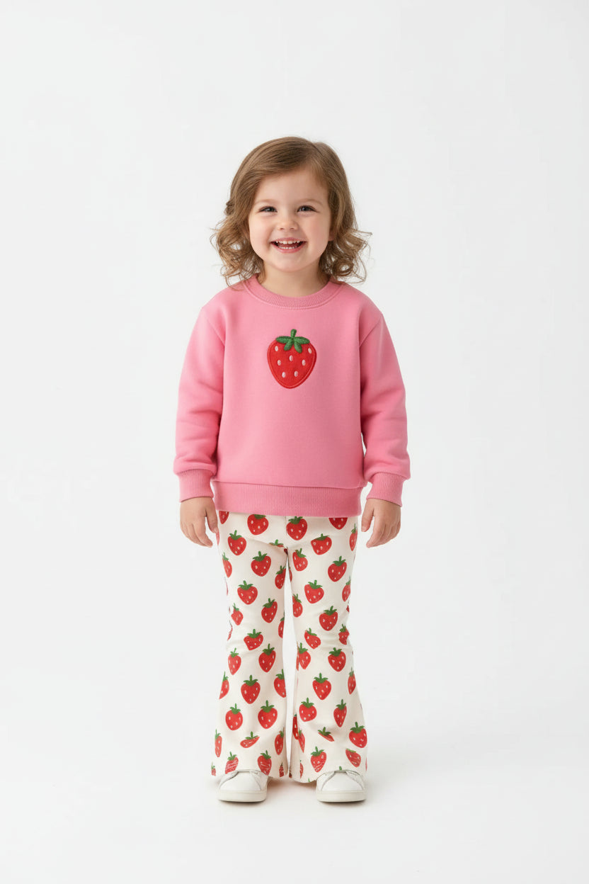 Pink sweatshirt with strawberry design and matching pants on a fur surface with flowers and shoes.