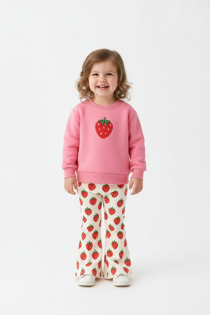 Pink sweatshirt with strawberry design and matching pants on a fur surface with flowers and shoes.