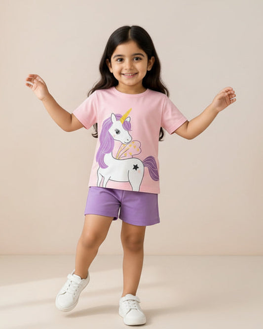 Child wearing a pink t-shirt with a unicorn design and purple shorts, standing in front of a 'Babies Corner' sign.